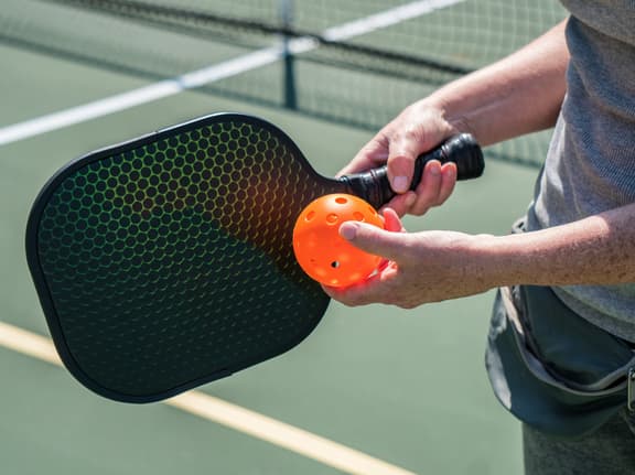 This is a photo of a man about to serve an orange ball on a pickleball court..