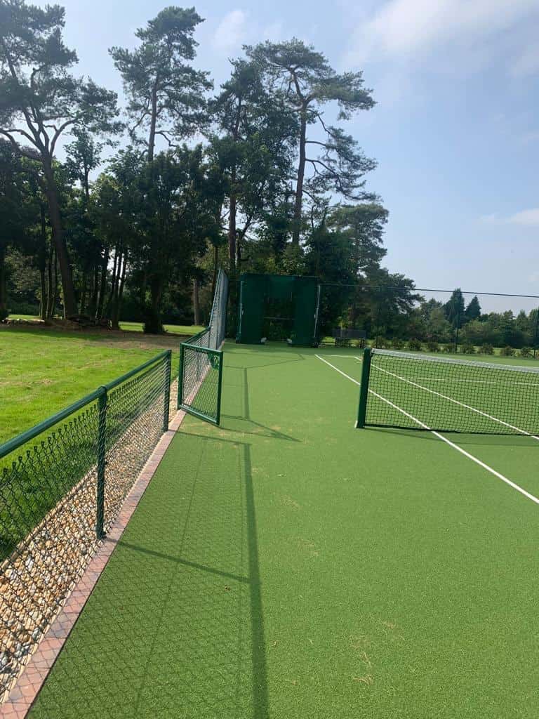 This is a photo of a new tennis court showing the green service with white lines, and also showing the entrance gate onto the court which is located in the middle by the service line.