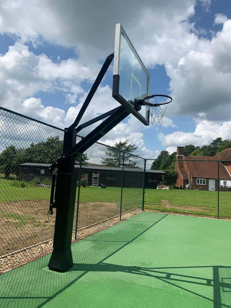 This is a photo of a basketball net at the edge of the tennis court by the fence. The court has just been installed.