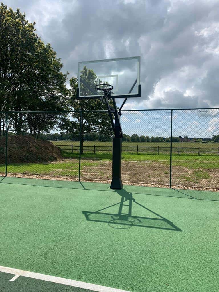 This is a photo of a basketball net at the edge of the tennis court by the fence. The court has just been installed.