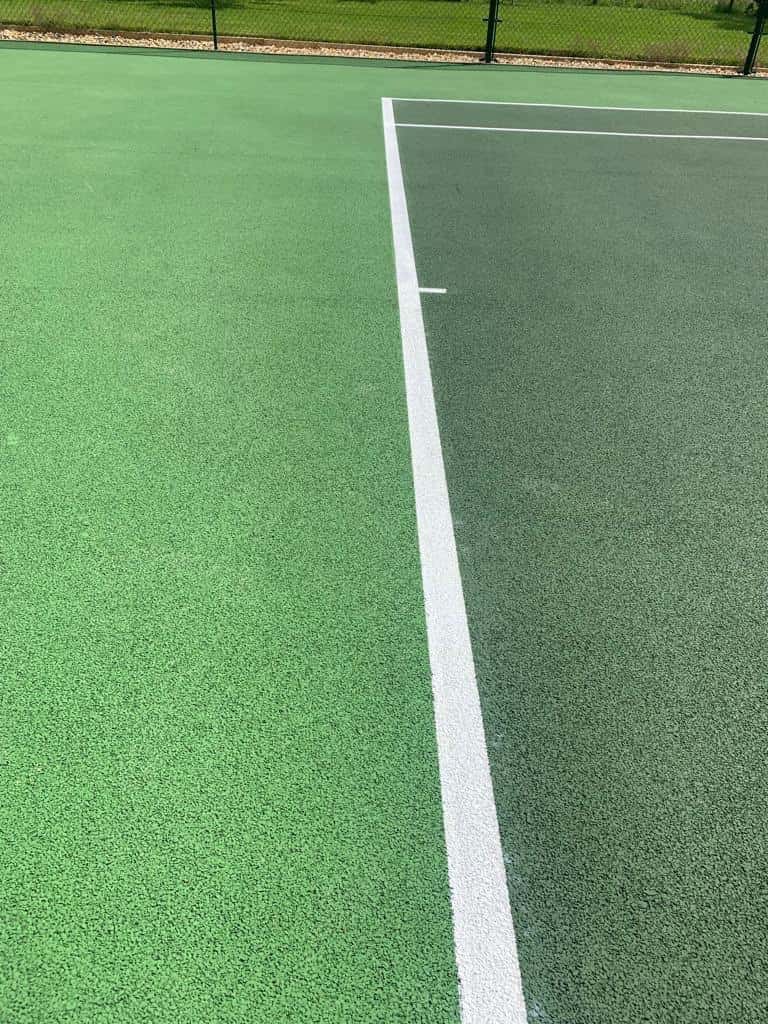 This is a photo of a tennis court surface showing the green finish and the white lines.