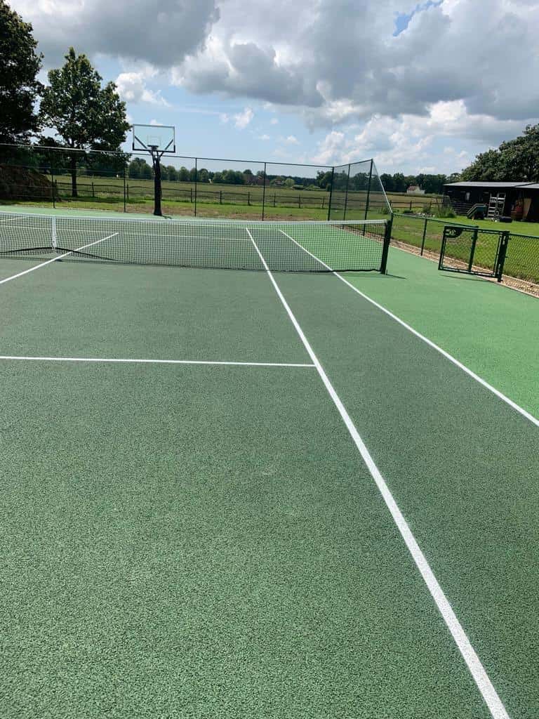 This is a photo of a tennis court that has just been installed. The photo is taking from the serving area of the court and shows the net and in the distance the fence, which also has a basket ball net. This could be classed as a MUGA court.