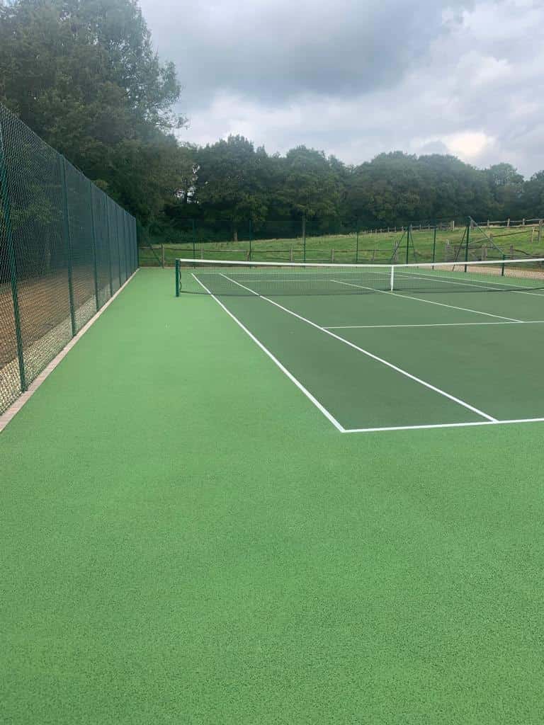 This is a photo of a new tennis court, which has recently been constructed. with a green fence, part of which is a tapered drop fence